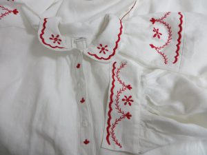 biała koszula z czerwonymi haftowanymi detalami.