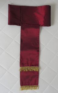 czerwony szalik z frędzlami na białej powierzchni.