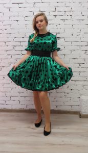 kobieta w zielonej sukience stojąca przed białą ścianą z cegły.