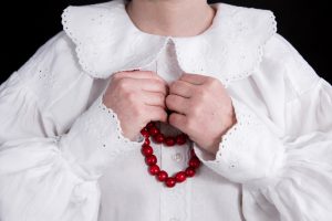 kobieta ubrana w białą koszulę i czerwony naszyjnik z koralików.