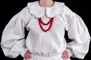 kobieta ubrana w białą bluzkę z czerwonym naszyjnikiem z koralików.