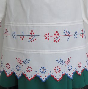 biała sukienka z czerwonymi, niebieskimi i zielonymi wykończeniami.